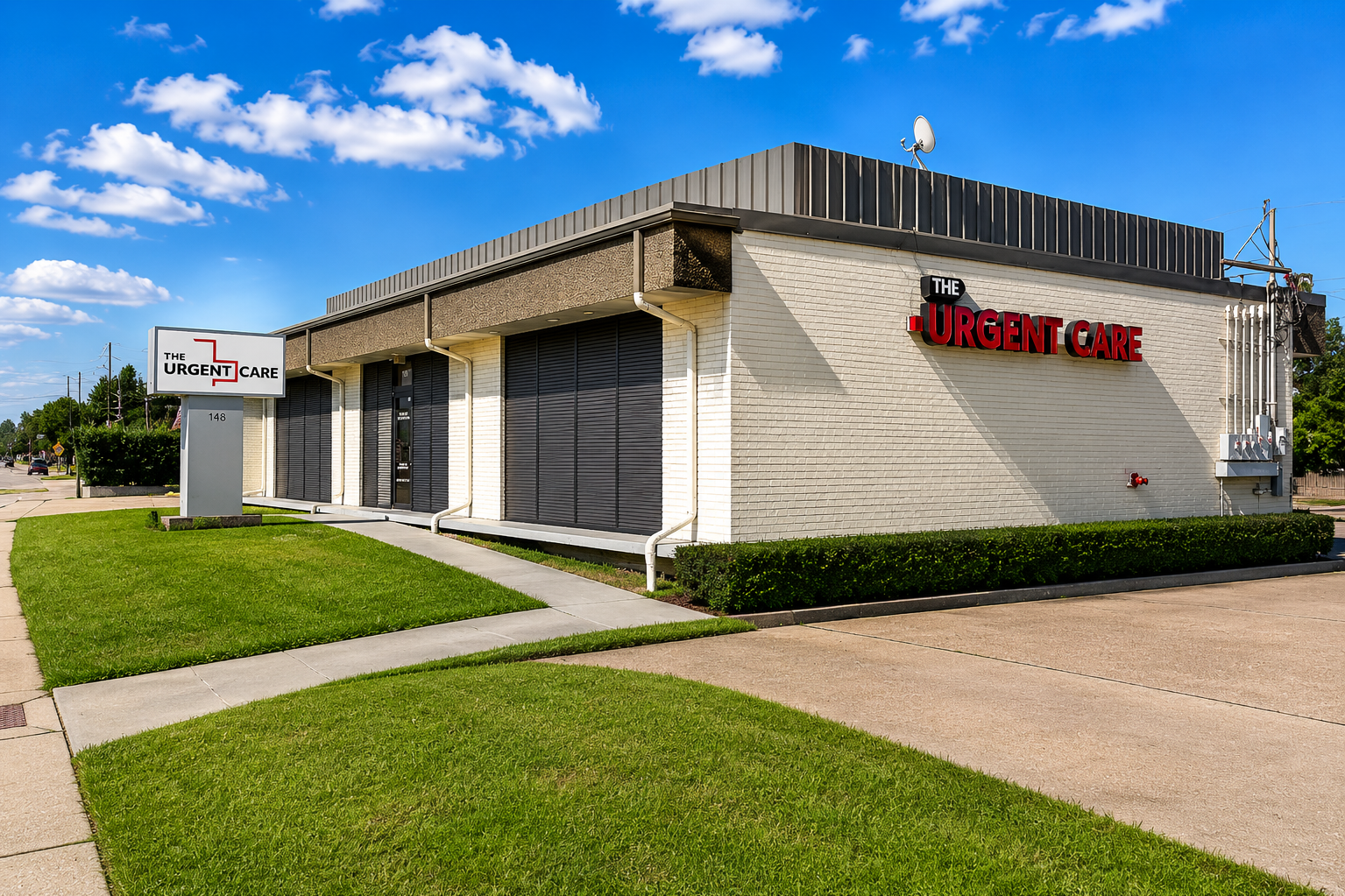 Urgent Care clinic exterior with bold red 'URGENT CARE' sign on white brick wall and manicured lawn nearby, under a blue sky.