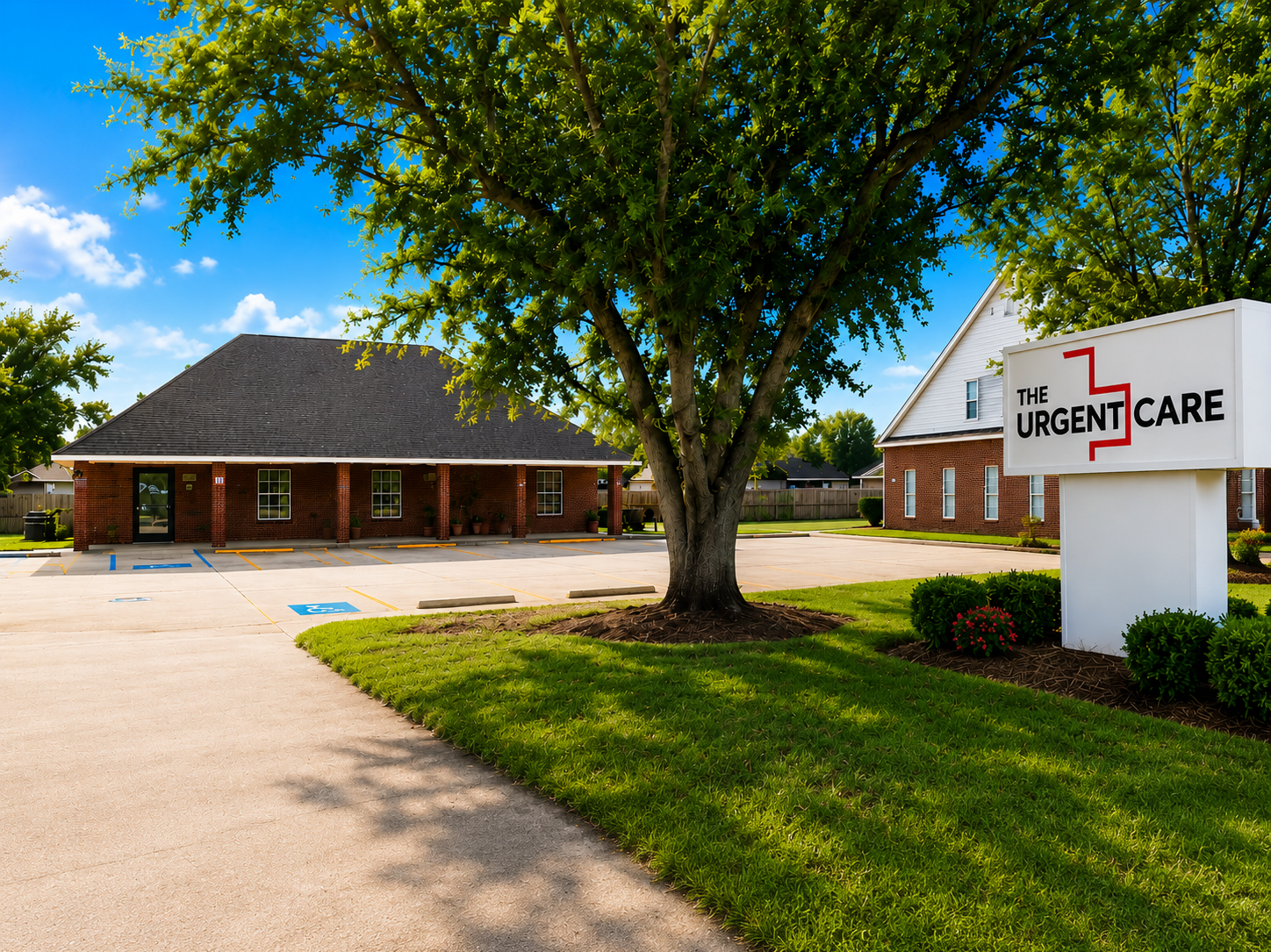 Front view of an urgent care clinic: brick building, large tree in the foreground, and a white sign reading 'The Urgent Care' beside the landscaping and parking lot.